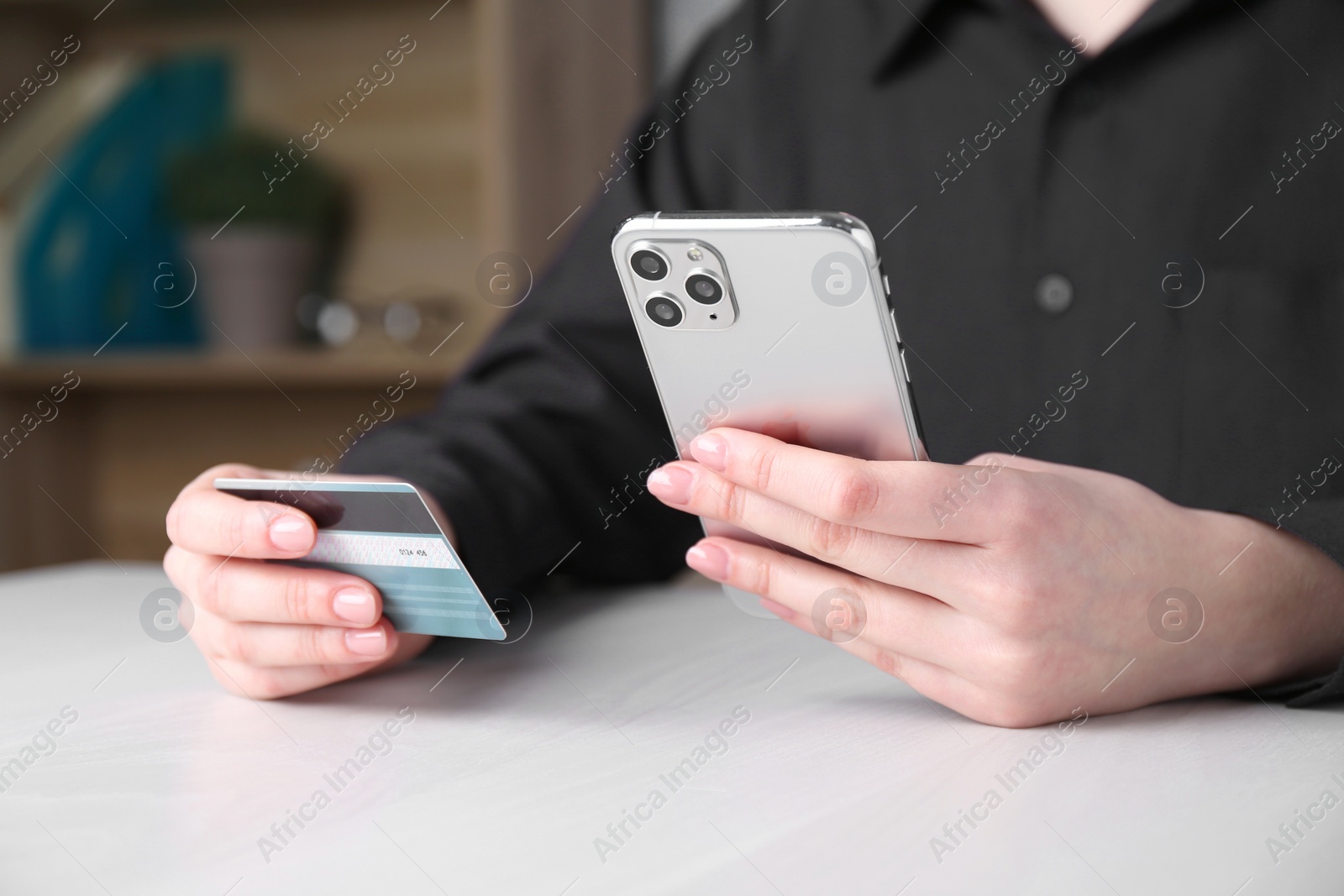 Photo of Online payment. Woman with smartphone and credit card at white wooden table, closeup