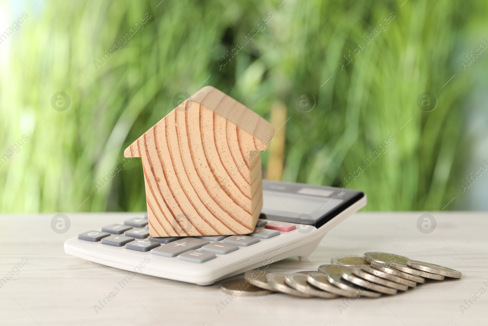 Photo of Wooden house model, calculator and coins on light table outdoors