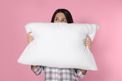 Young woman covering face with soft pillow on pink background