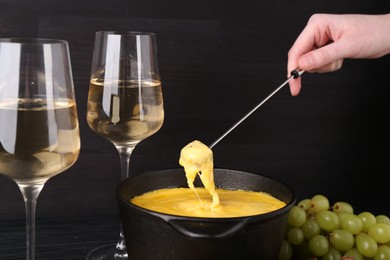 Photo of Woman dipping piece of bread into fondue pot with melted cheese at table, closeup