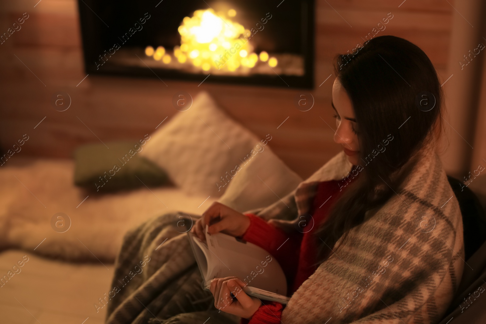 Photo of Woman reading book near decorative fireplace at home. Winter season