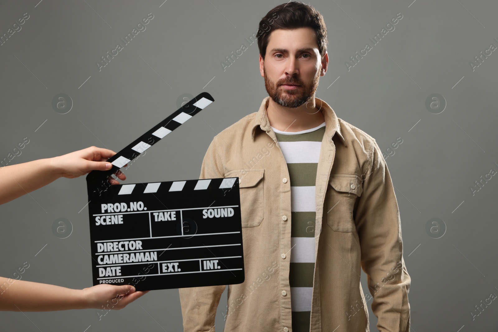 Photo of Actor performing while second assistant camera holding clapperboard on grey background