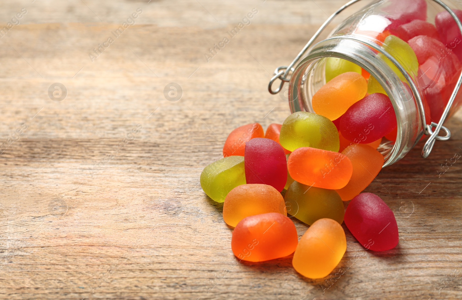 Photo of Glass jar and scattered jelly candies on wooden table, space for text