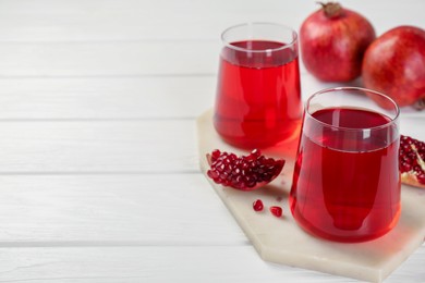 Photo of Tasty pomegranate juice in glasses and fresh fruits on white wooden table, closeup. Space for text
