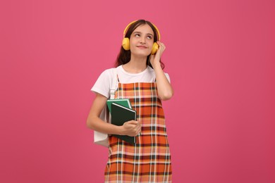 Teenage student with backpack, books and headphones listening to music on pink background
