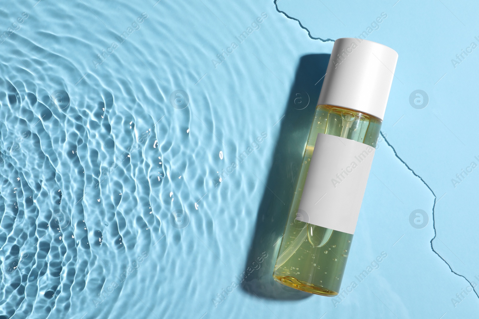 Photo of Bottle of cosmetic oil in water on light blue background, top view. Space for text
