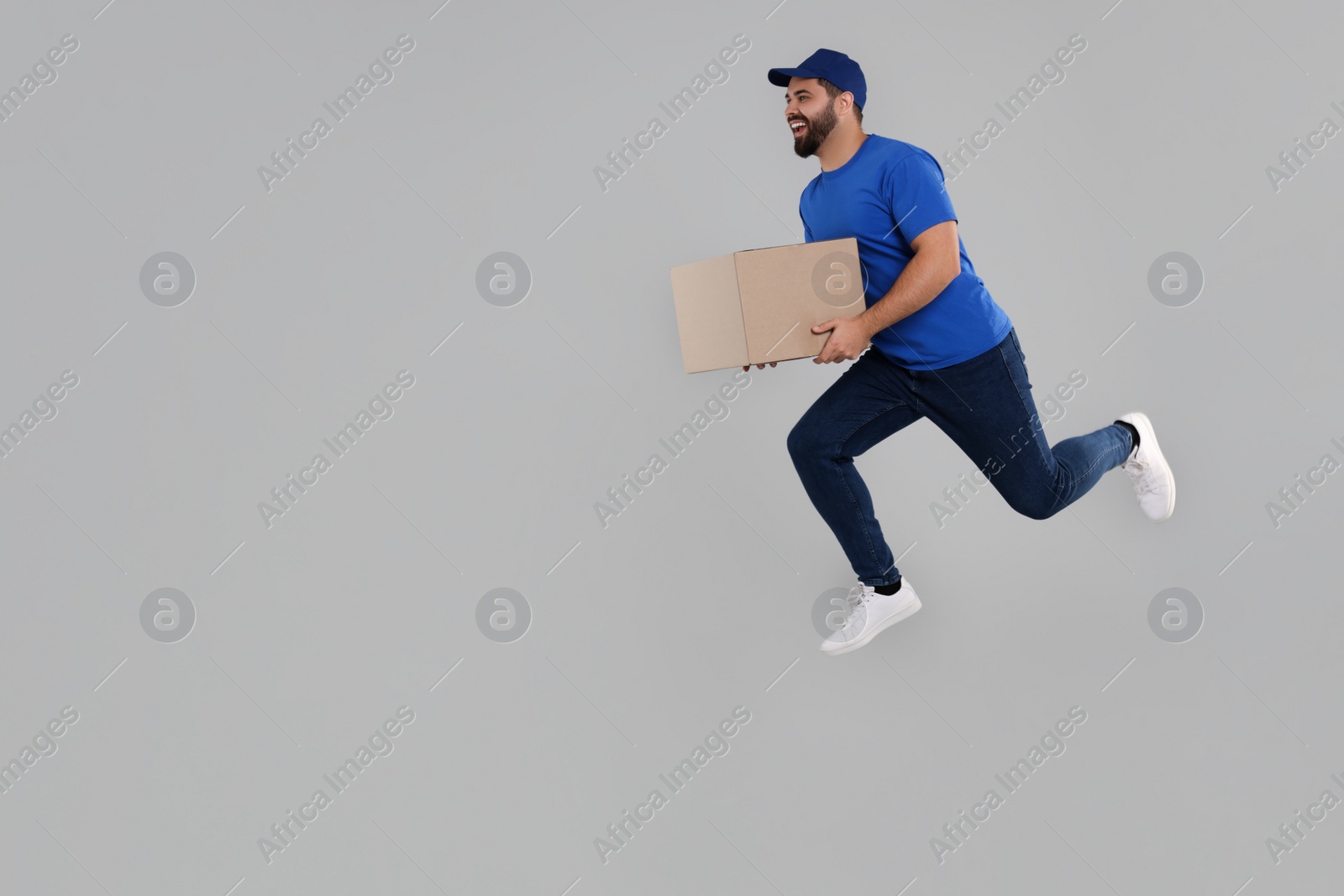Photo of Happy young courier running to deliver parcel on grey background, space for text