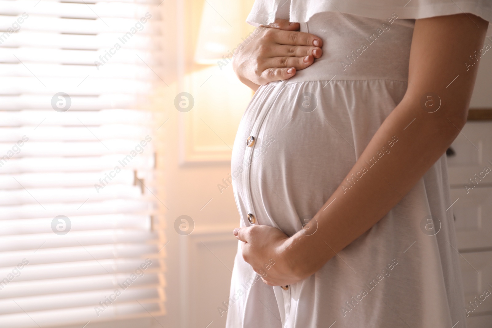 Photo of Pregnant young woman touching belly at home, closeup. Space for text