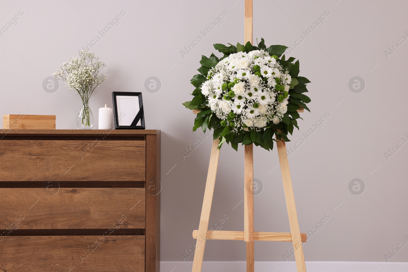 Photo of Wreath of flowers and frame with black ribbon on commode in room. Funeral attributes