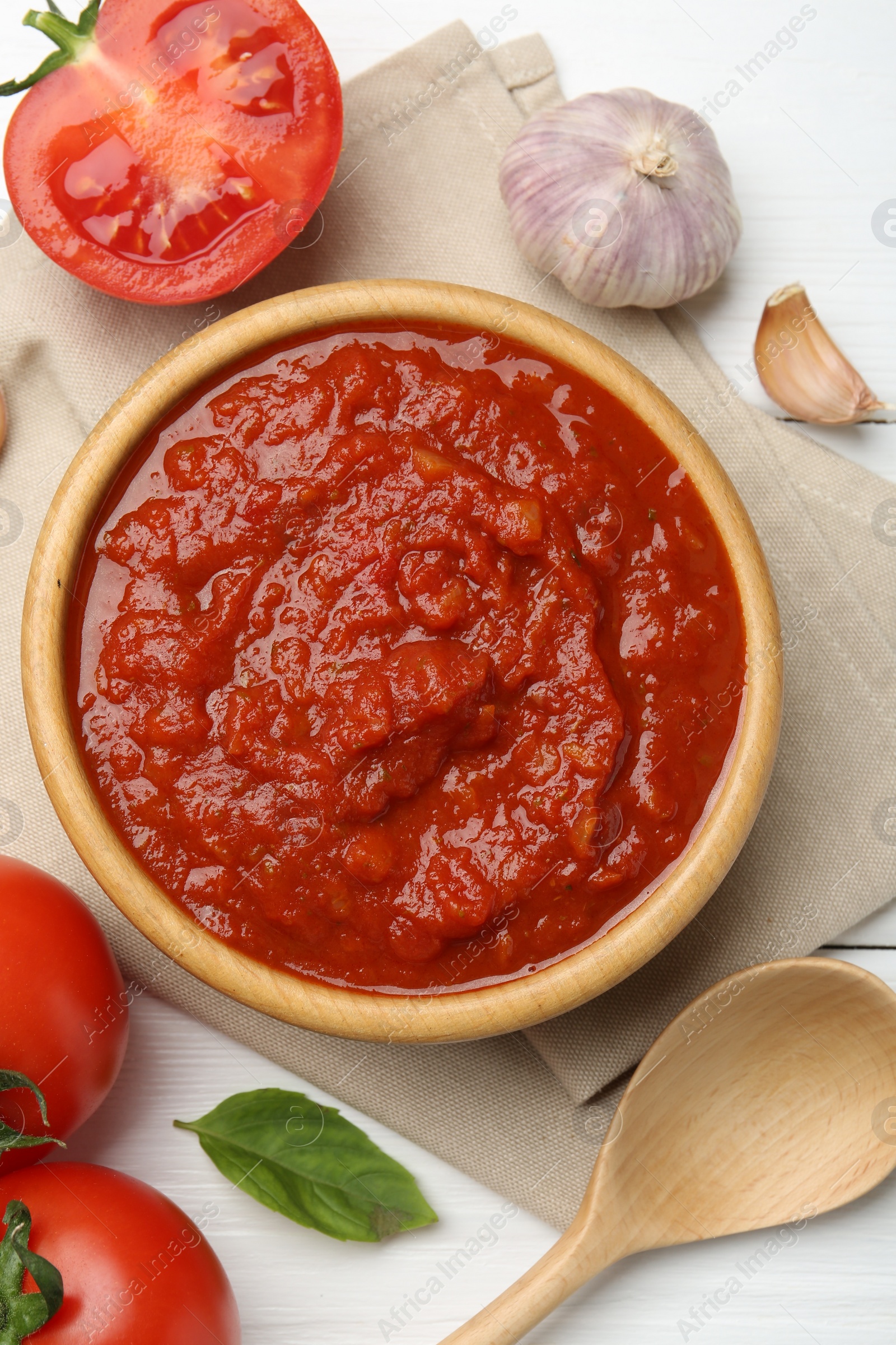 Photo of Homemade tomato sauce in bowl, spoon and fresh ingredients on white wooden table, flat lay