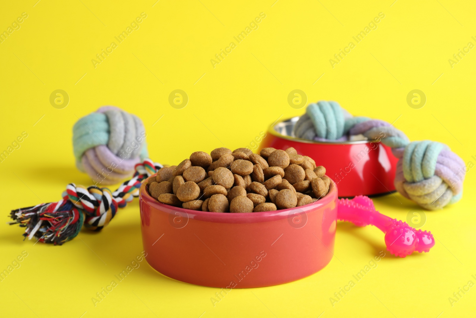 Photo of Feeding bowls and toys for pet on yellow background