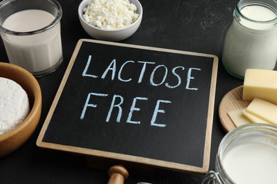 Photo of Dairy products and board with phrase Lactose free on black textured table