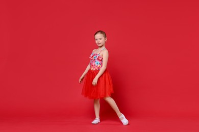 Photo of Cute little girl dancing on red background