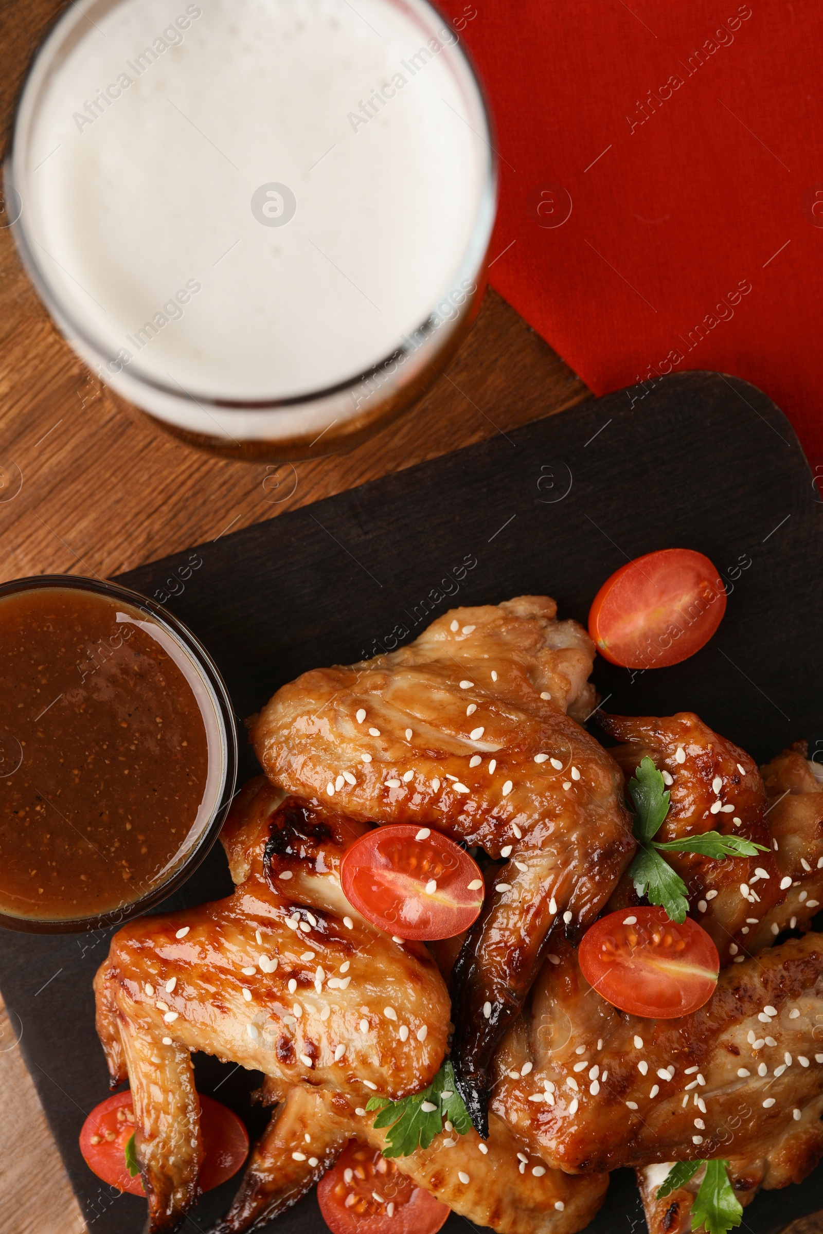 Photo of Glass of beer, delicious baked chicken wings and sauce on wooden table, flat lay