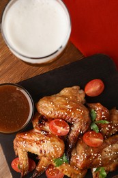 Photo of Glass of beer, delicious baked chicken wings and sauce on wooden table, flat lay