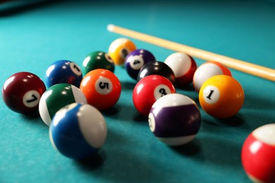 Many colorful billiard balls and cue on green table, closeup