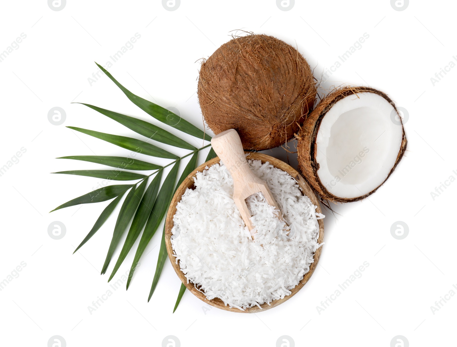 Photo of Coconut flakes in bowl, scoop, nuts and palm leaf isolated on white, top view