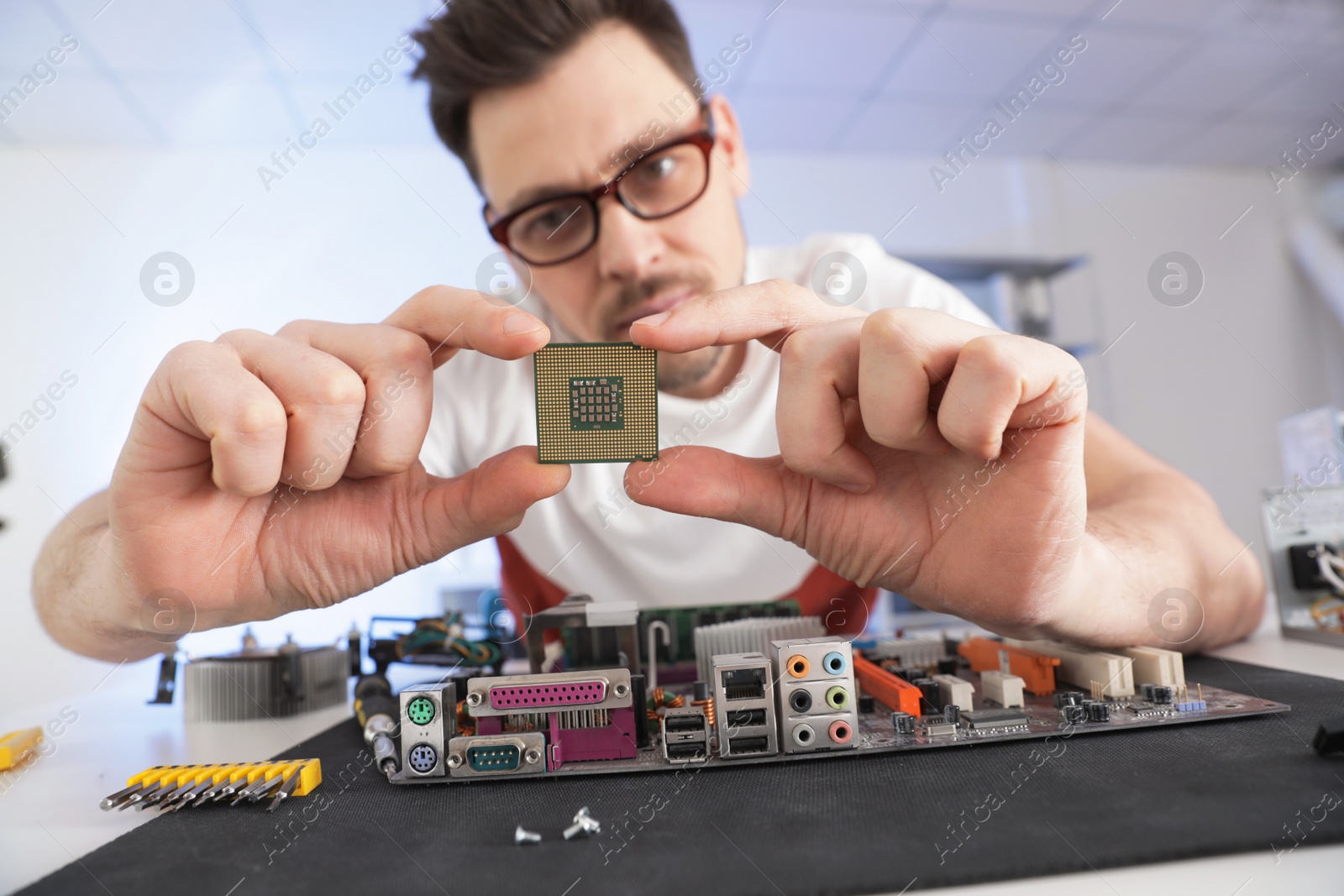 Photo of Male technician repairing motherboard at table indoors