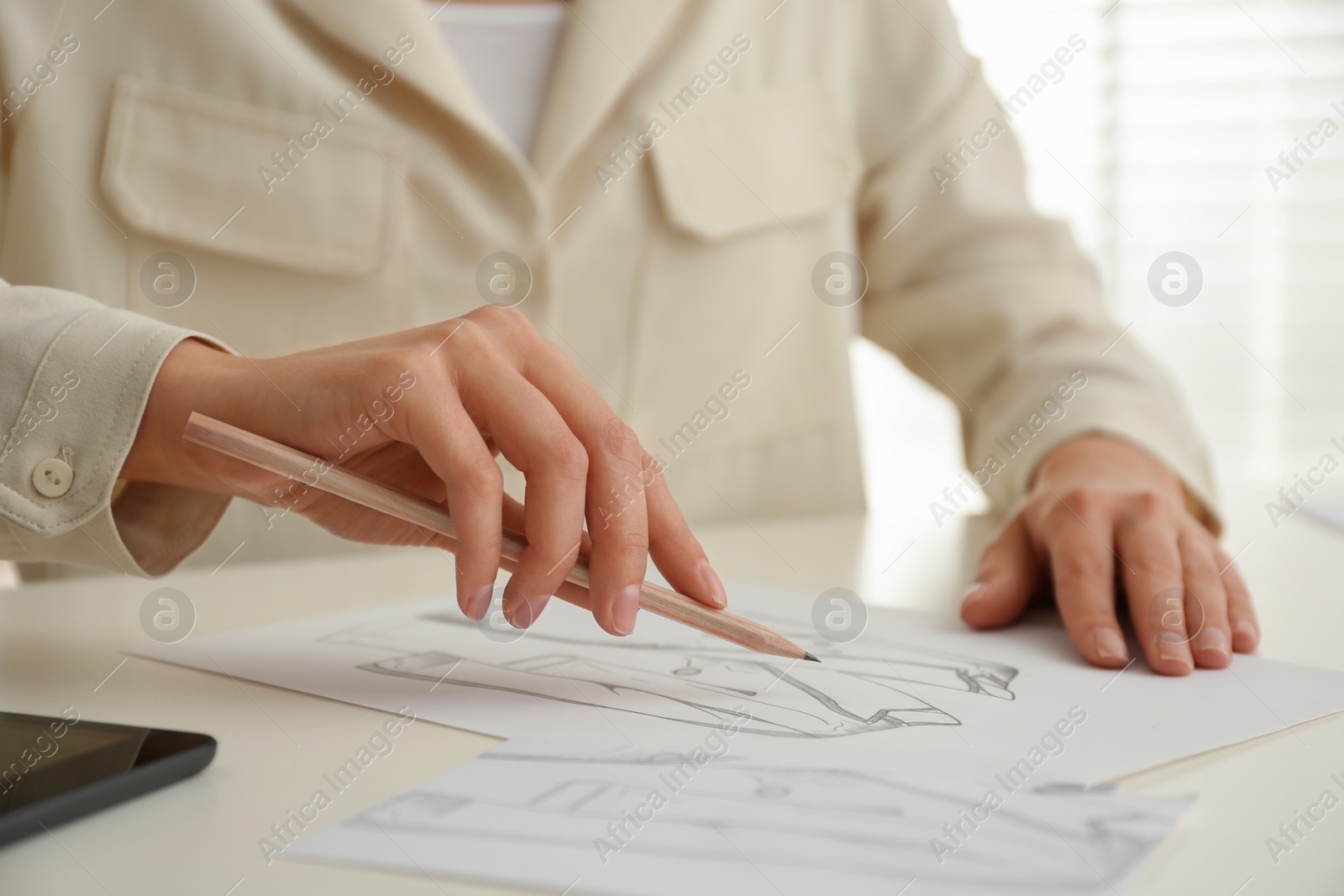 Photo of Woman drawing clothes with pencil on sheet of paper at white table, closeup