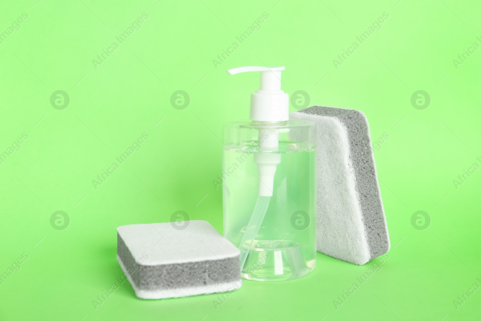 Photo of Bottle of detergent and sponges on green background