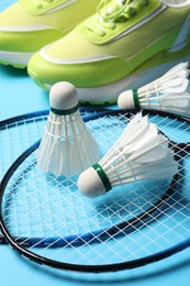 Photo of Feather badminton shuttlecocks, rackets and sneakers on light blue background, closeup