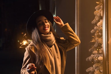 Photo of Woman in warm clothes holding burning sparkler outdoors