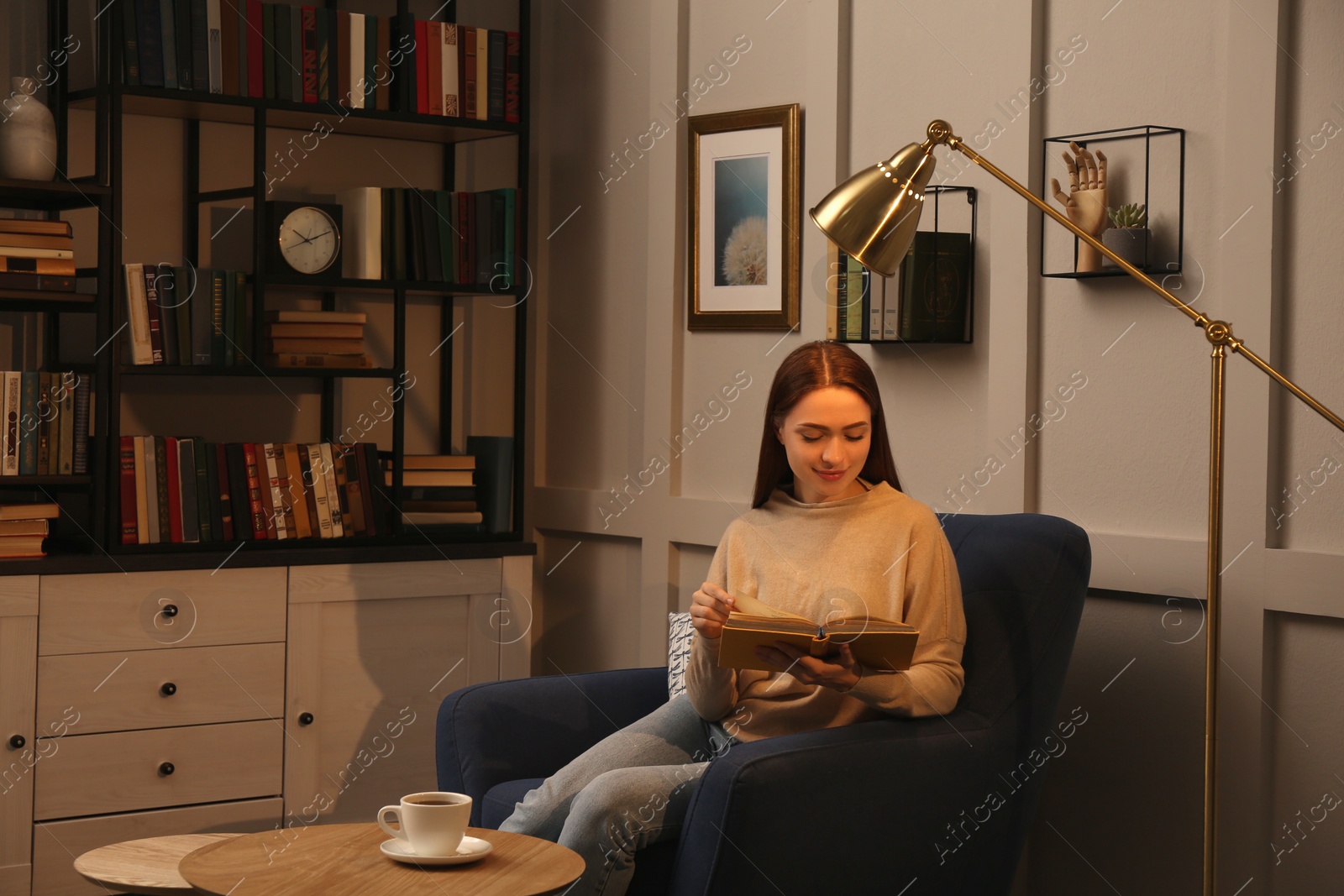 Photo of Young woman reading book in armchair indoors. Home library