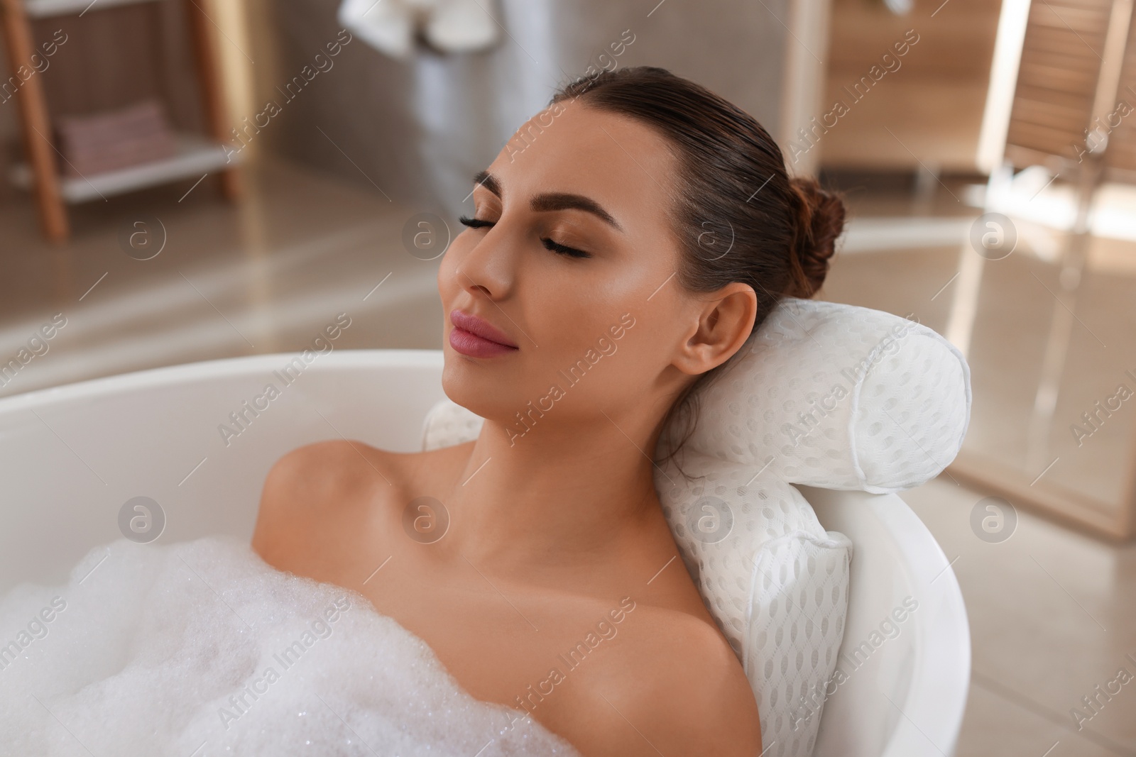 Photo of Young woman using pillow while enjoying bubble bath indoors