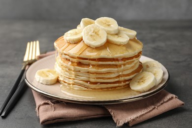 Photo of Tasty pancakes with sliced banana and honey served on gray table, closeup