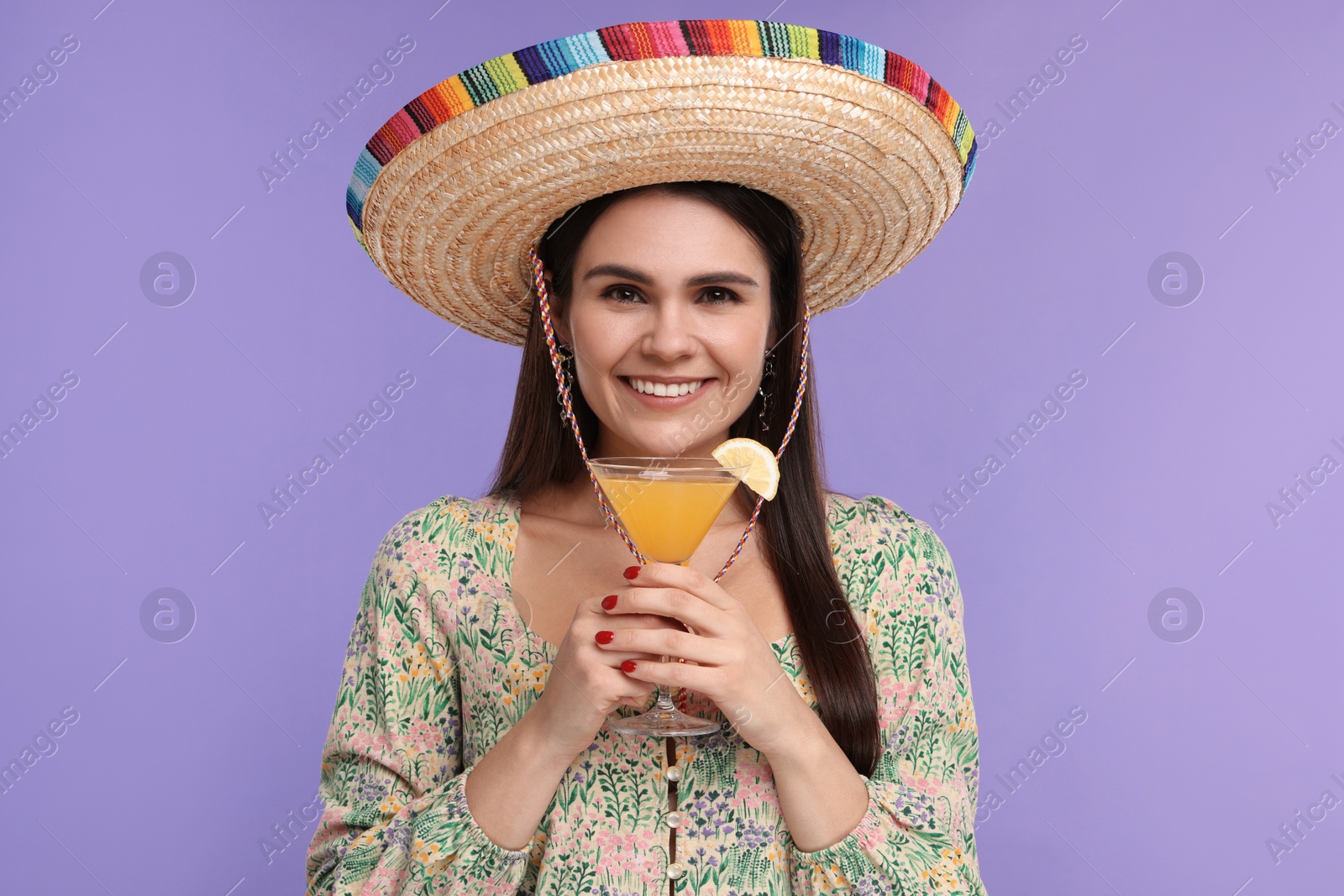 Photo of Young woman in Mexican sombrero hat with cocktail on violet background