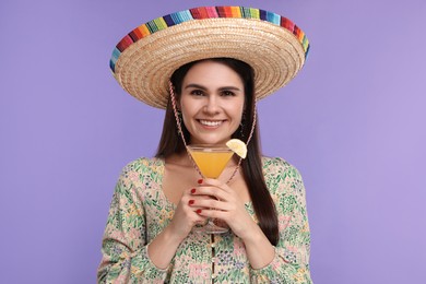Photo of Young woman in Mexican sombrero hat with cocktail on violet background