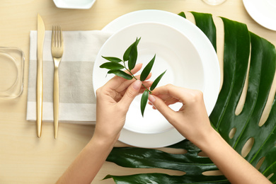 Photo of Woman setting table with green leaves for festive dinner, top view