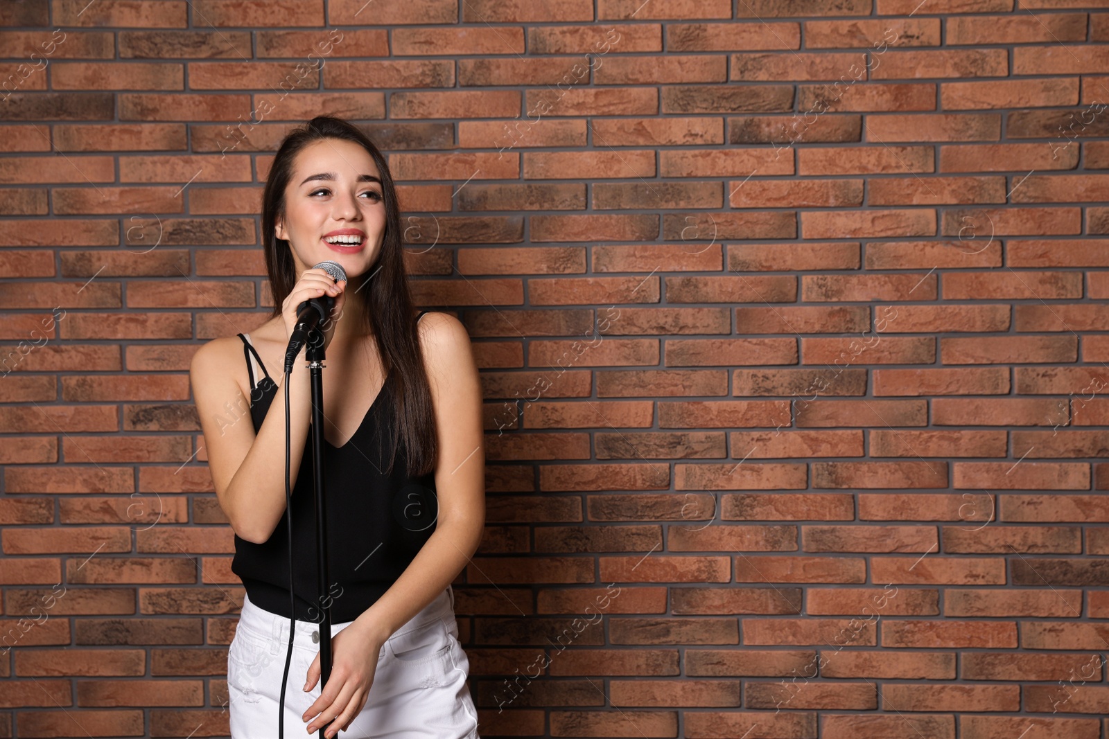 Photo of Young stylish woman posing with microphone near brick wall. Space for text