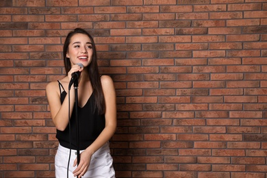 Young stylish woman posing with microphone near brick wall. Space for text