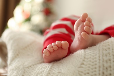 Photo of Cute little baby on knitted blanket in room with Christmas tree, closeup