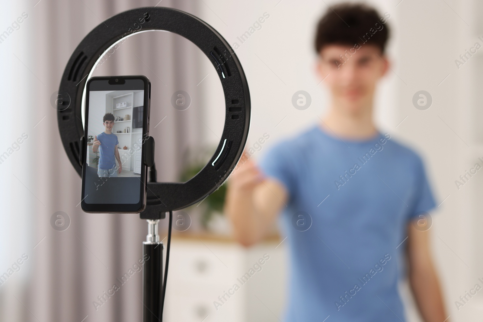 Photo of Teenage blogger explaining something while streaming at home, focus on smartphone