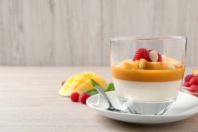 Photo of Delicious panna cotta with mango coulis, fresh fruit pieces and almond flakes on light wooden table. Space for text