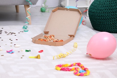 Photo of Pizza box with leftovers on messy apartment floor. After party chaos