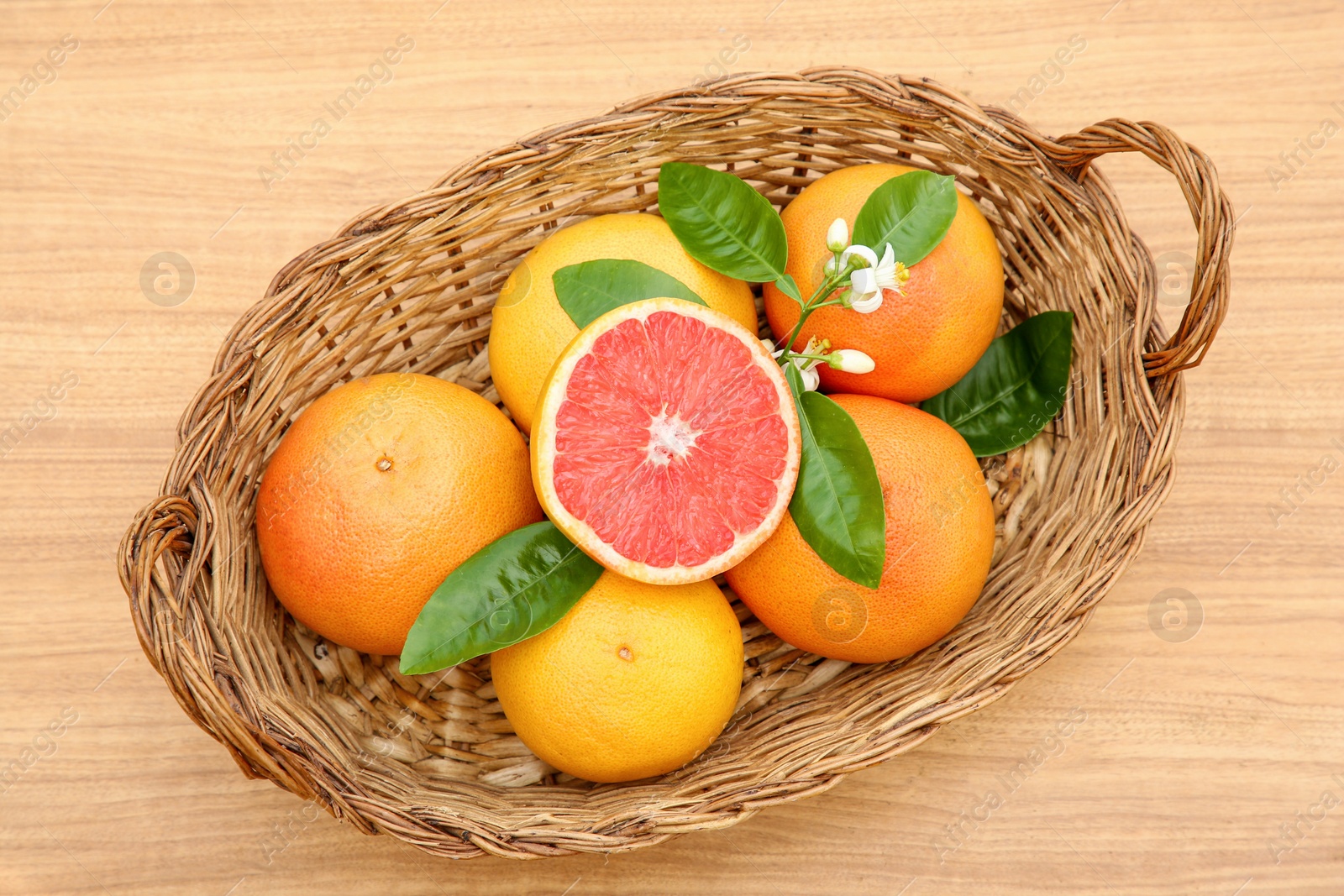 Photo of Wicker basket with fresh ripe grapefruits and green leaves on wooden table, top view