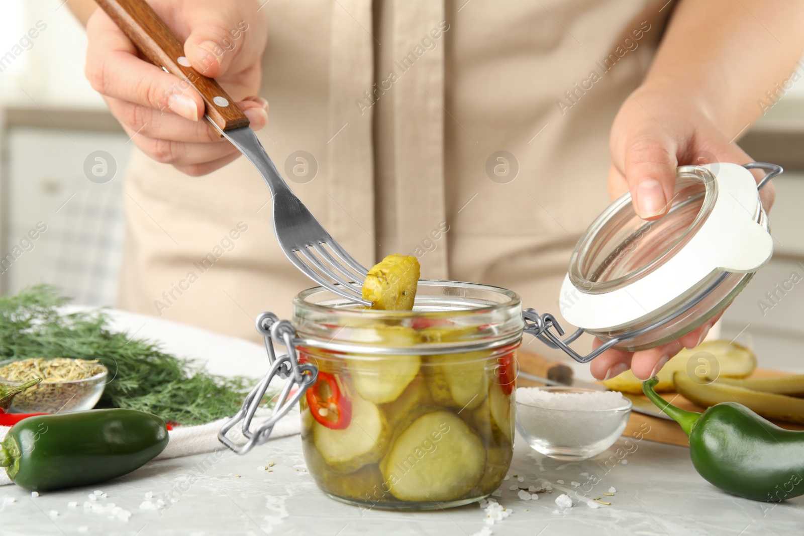 Photo of Woman taking pickled cucumber from jar at table in kitchen, closeup view