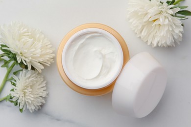 Photo of Jar of face cream and flowers on white marble table, flat lay