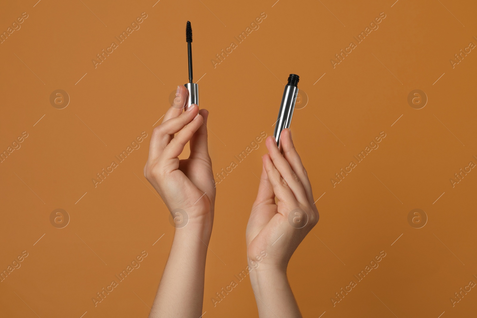 Photo of Woman holding mascara for eyelashes on light brown background, closeup