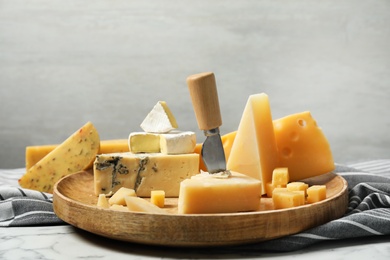 Wooden plate with different types of delicious cheese on marble table against light background