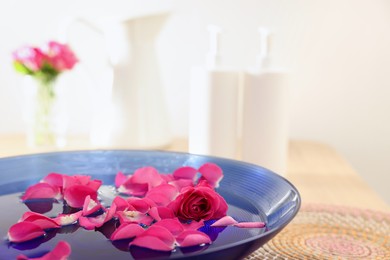 Photo of Pink roses and petals in bowl with water on table, closeup. Space for text