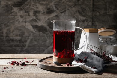 Freshly brewed hibiscus tea in teapot and dry flower petals on wooden table. Space for text