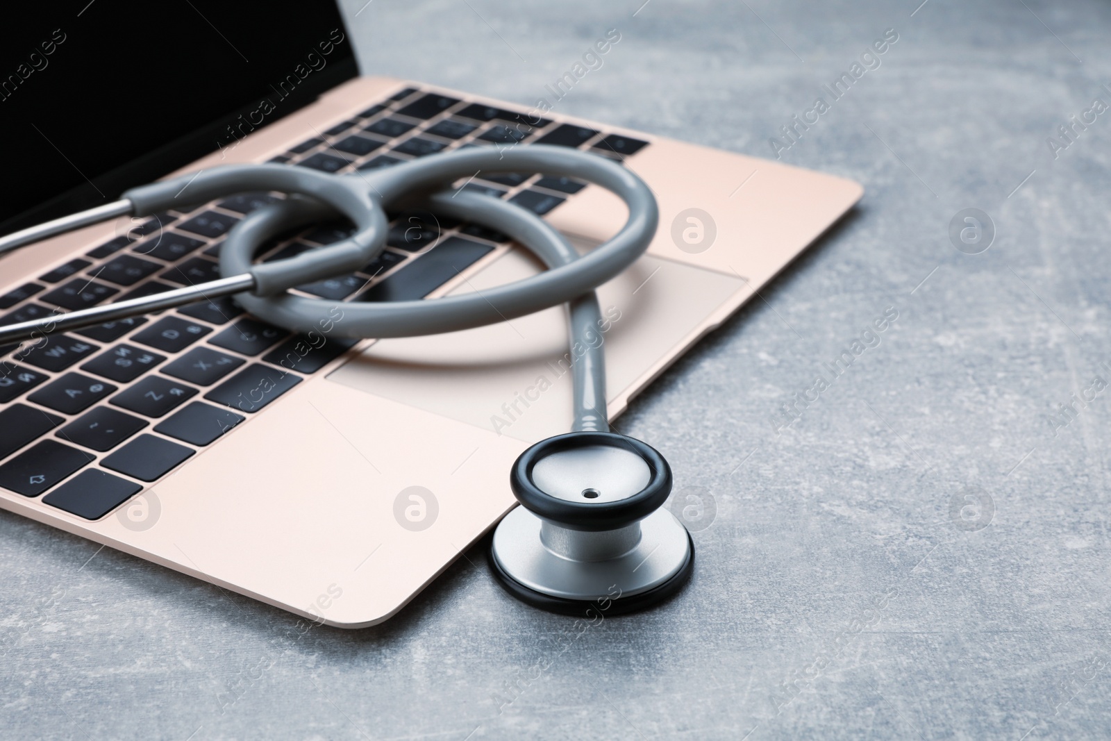 Photo of Laptop with stethoscope on grey table, closeup. Space for text