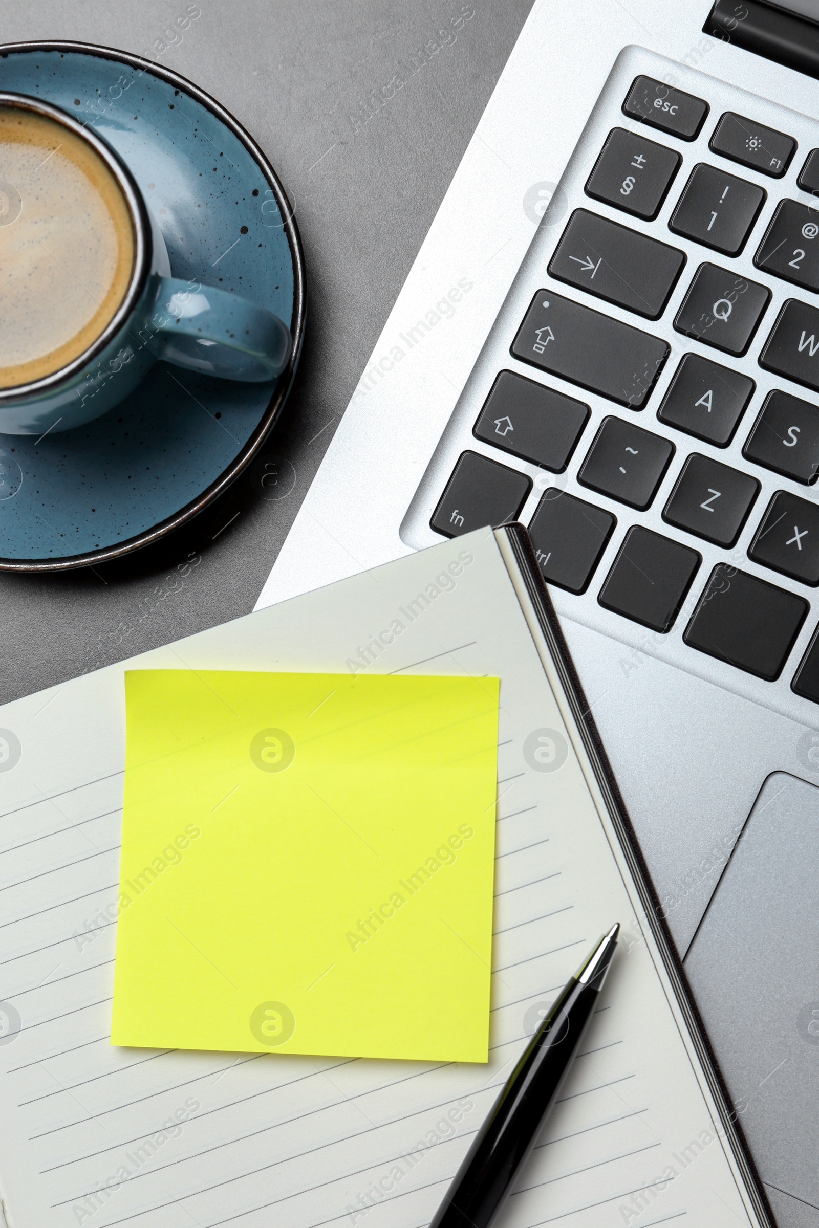 Photo of Laptop, planner, empty sticky note, pen and cup of coffee on grey table, flat lay. Space for design