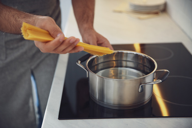 Photo of Man cooking pasta on stove in kitchen, closeup