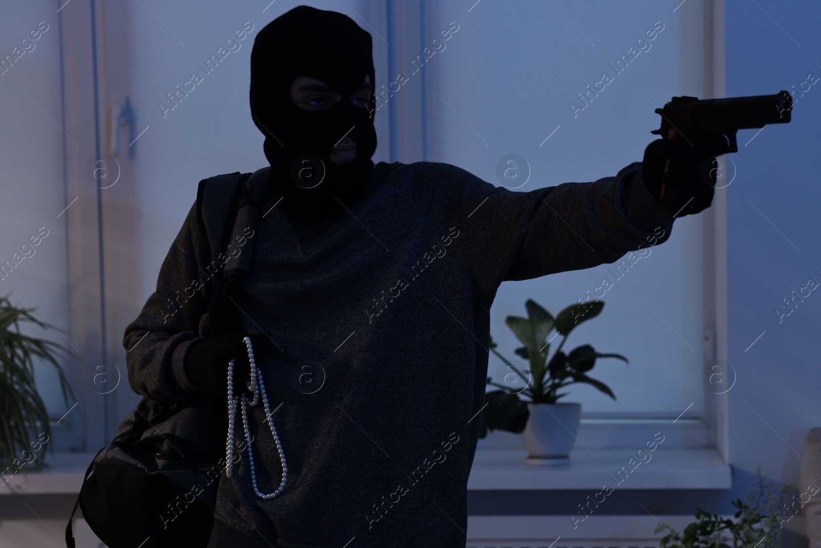 Photo of Thief with gun stealing jewels in foreign house. Burglary