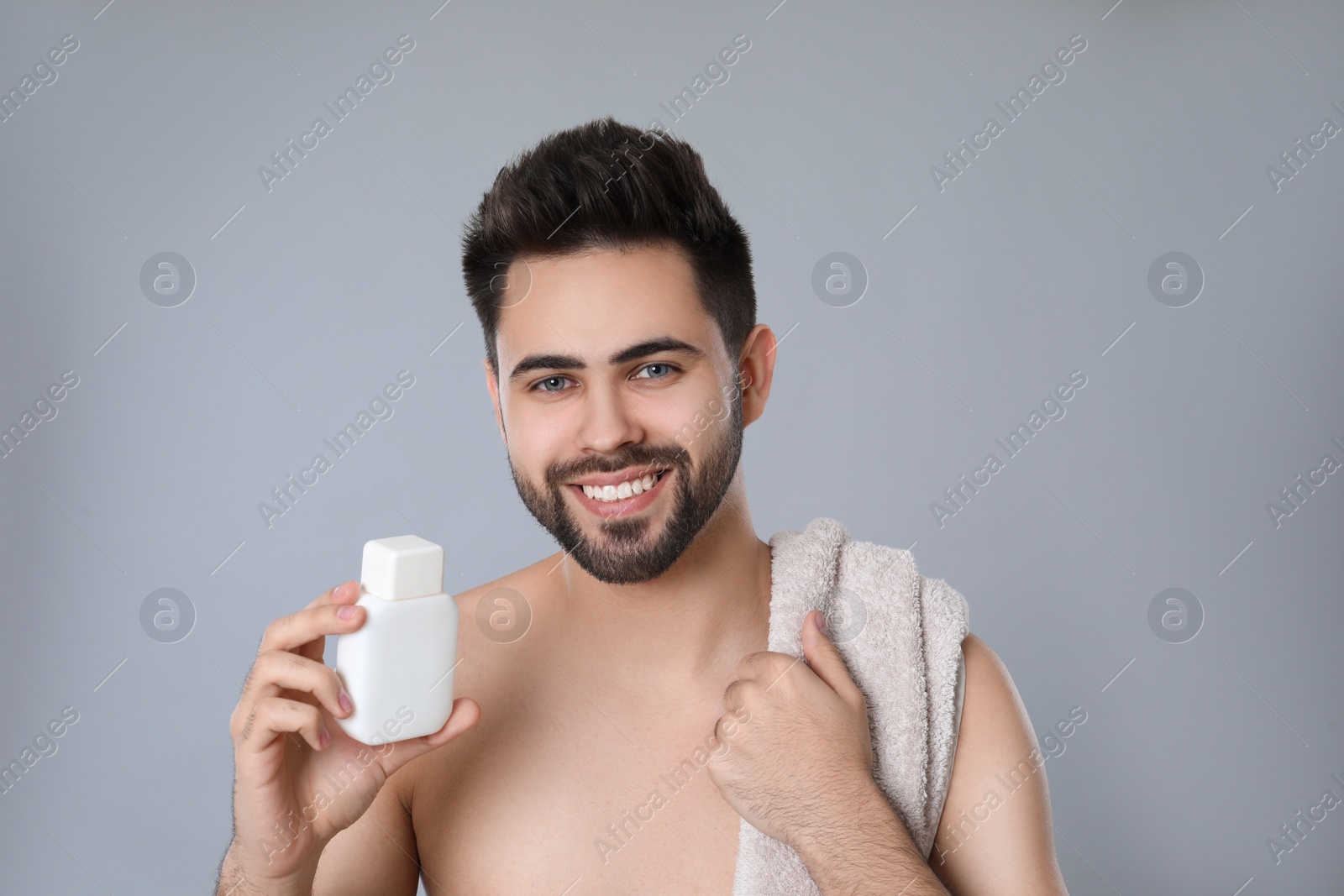 Photo of Handsome young man with beard holding post shave lotion on grey background